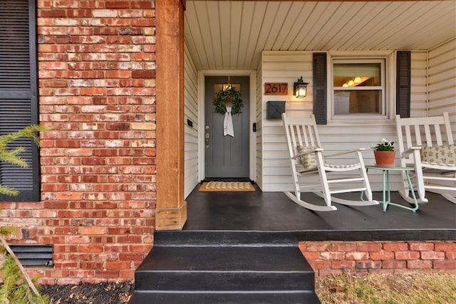 doorway to property with covered porch and brick siding