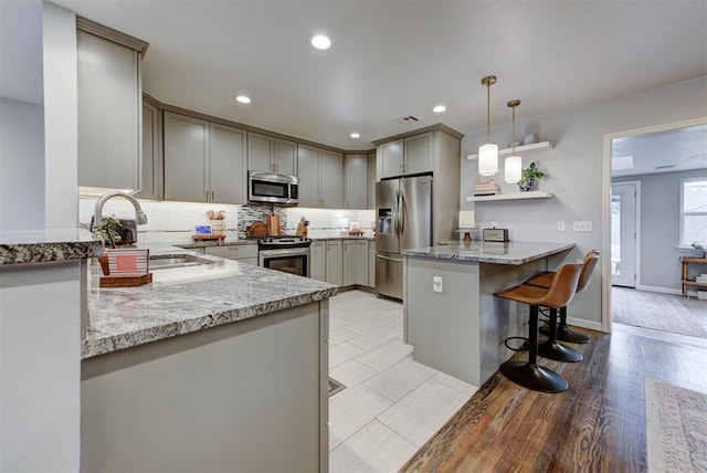 kitchen with gray cabinetry, a peninsula, a sink, appliances with stainless steel finishes, and tasteful backsplash