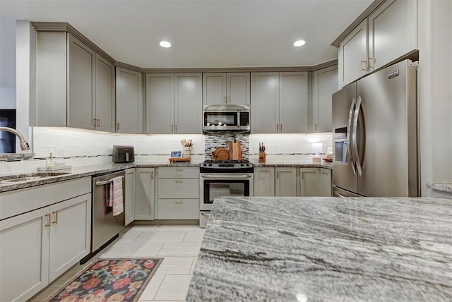 kitchen featuring light stone counters, stainless steel appliances, recessed lighting, decorative backsplash, and a sink