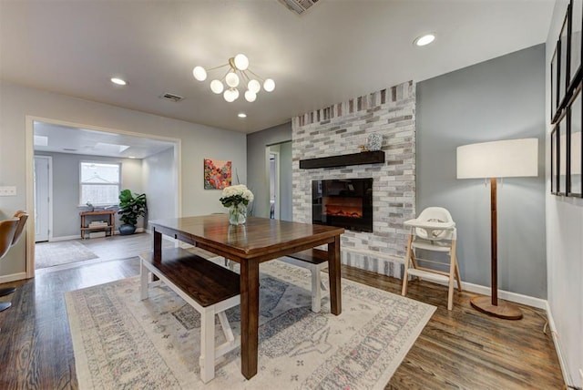 dining room with a brick fireplace, visible vents, baseboards, and wood finished floors