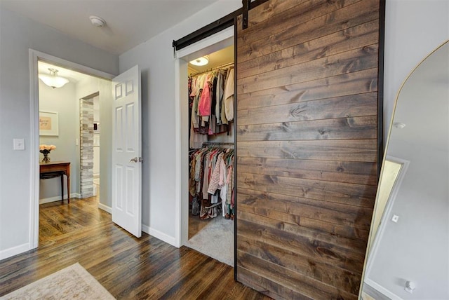 corridor featuring dark wood finished floors, baseboards, and a barn door