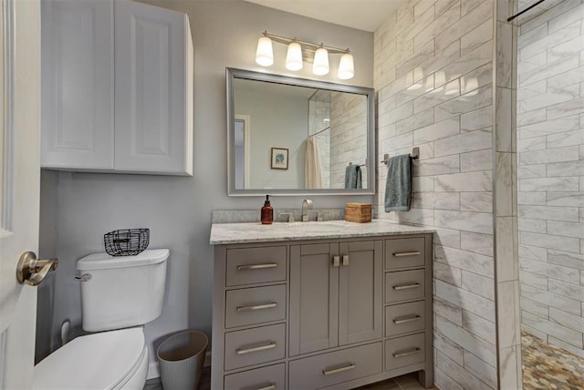 bathroom featuring toilet, tiled shower, and vanity