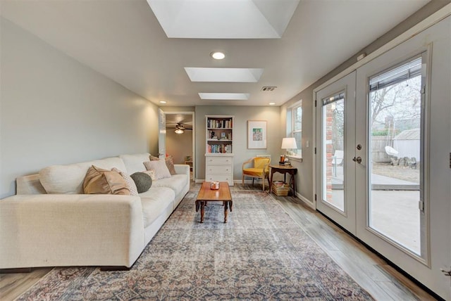 living area featuring a skylight, baseboards, visible vents, wood finished floors, and french doors