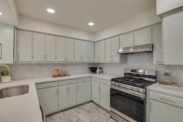 kitchen with decorative backsplash, stainless steel range with gas stovetop, light countertops, under cabinet range hood, and a sink