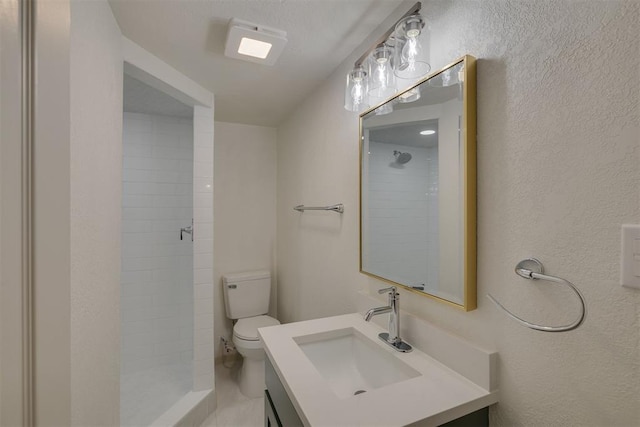 bathroom featuring a textured wall, a tile shower, vanity, and toilet