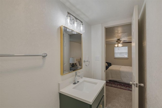 ensuite bathroom with a textured wall, ceiling fan, vanity, ensuite bath, and a textured ceiling