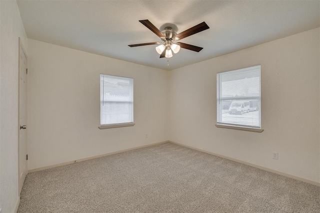 carpeted spare room featuring a ceiling fan and baseboards