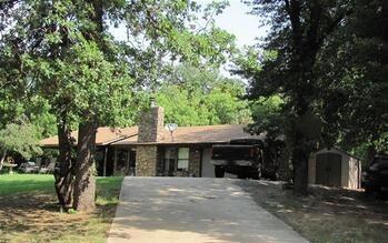 view of front facade with a chimney, driveway, a storage unit, and an outbuilding