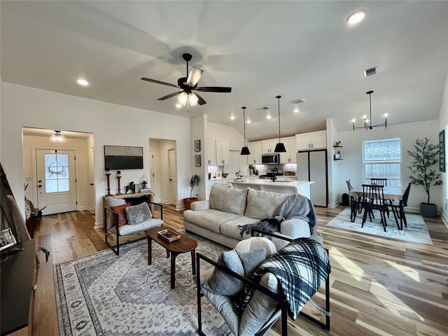 living room with lofted ceiling, a healthy amount of sunlight, light wood-style flooring, and ceiling fan with notable chandelier