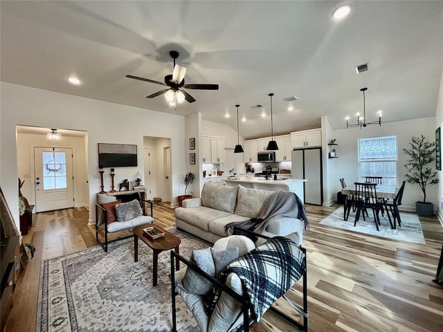 living room featuring visible vents, light wood-style flooring, ceiling fan with notable chandelier, vaulted ceiling, and recessed lighting