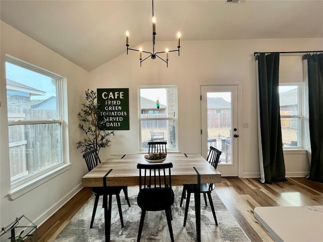 dining room featuring lofted ceiling, wood finished floors, a wealth of natural light, and an inviting chandelier