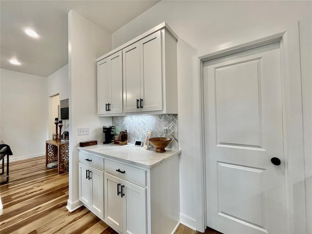 kitchen featuring baseboards, backsplash, light wood-style flooring, and white cabinetry