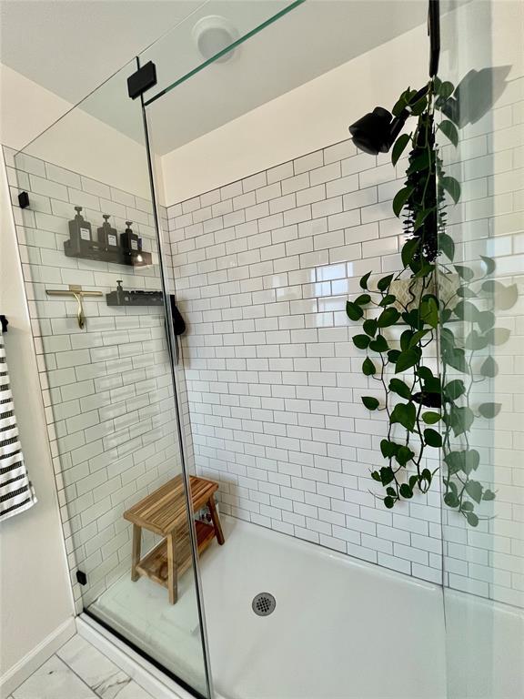 full bathroom with marble finish floor, a stall shower, and baseboards