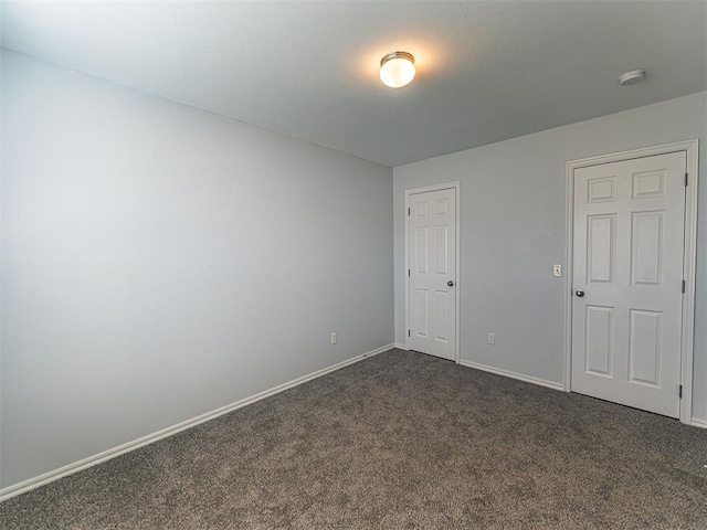 spare room featuring dark colored carpet and baseboards