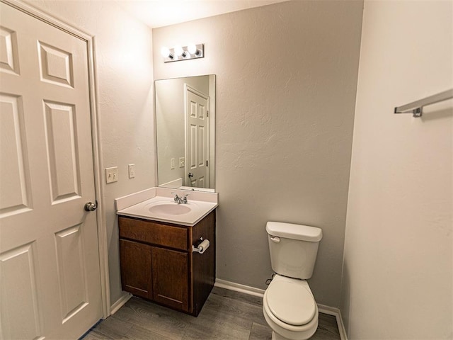 half bathroom with wood finished floors, vanity, toilet, and baseboards