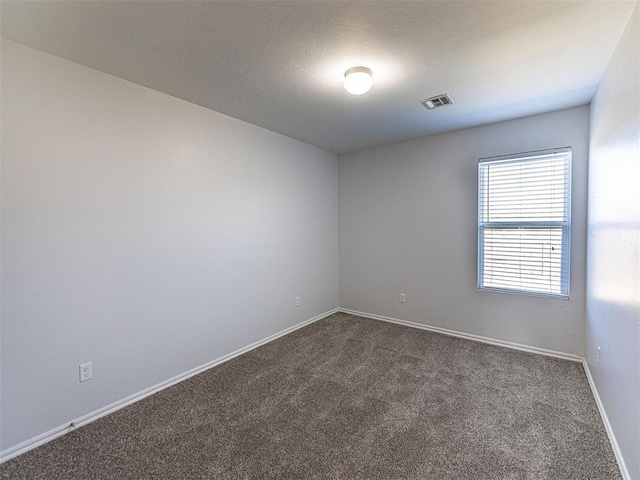 unfurnished room featuring visible vents, dark carpet, and baseboards