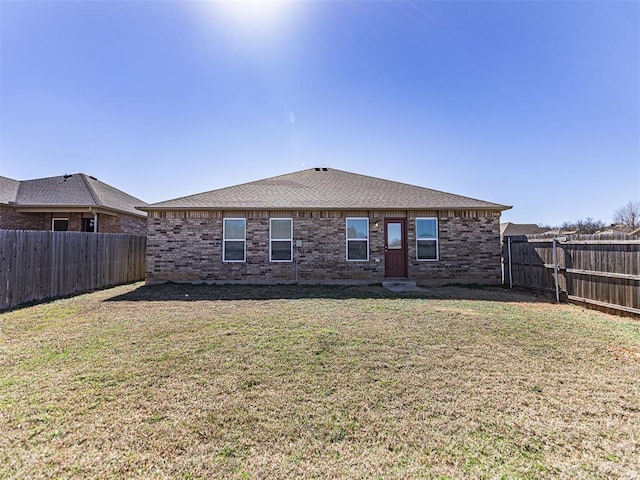 rear view of property featuring roof with shingles, brick siding, a lawn, and a fenced backyard