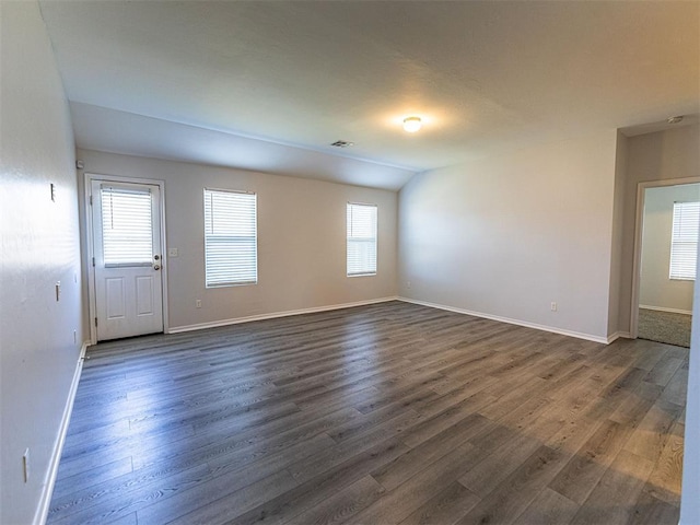 spare room featuring vaulted ceiling, dark wood-type flooring, visible vents, and baseboards