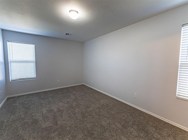 unfurnished room featuring baseboards, visible vents, and dark colored carpet