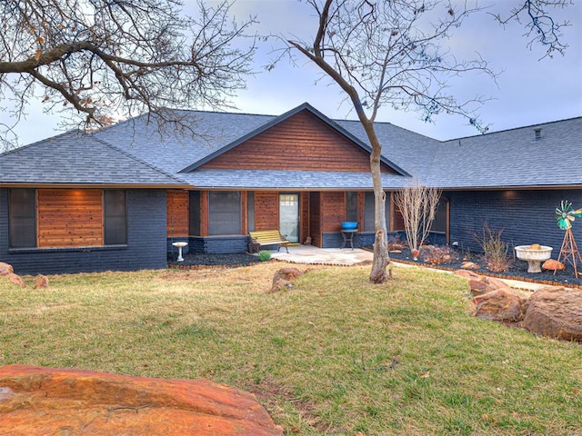 view of front of property featuring roof with shingles, a front lawn, and brick siding