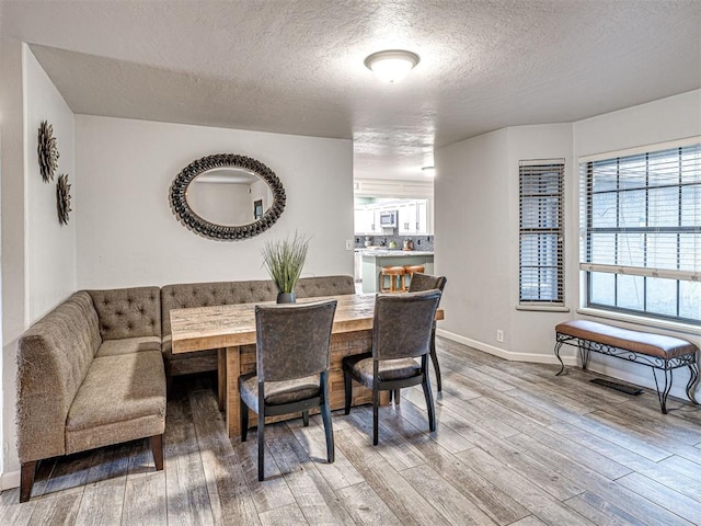 dining area with light wood finished floors, baseboards, and a textured ceiling