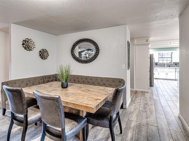 dining area with light wood finished floors, baseboards, and a textured ceiling