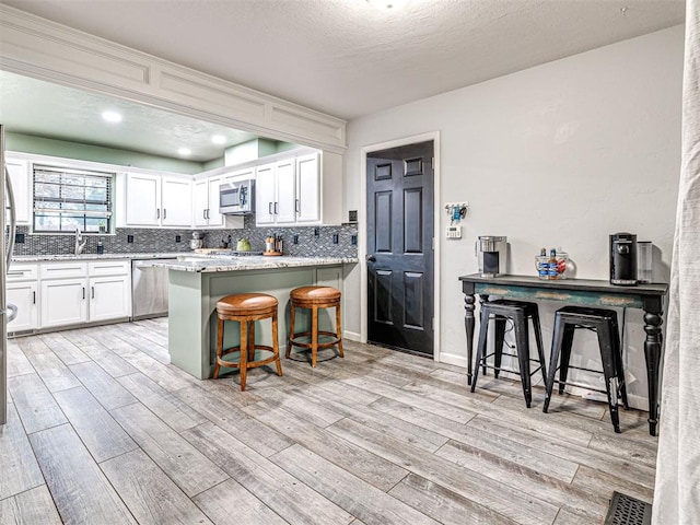 kitchen with white cabinetry, a kitchen breakfast bar, light wood-style floors, appliances with stainless steel finishes, and decorative backsplash