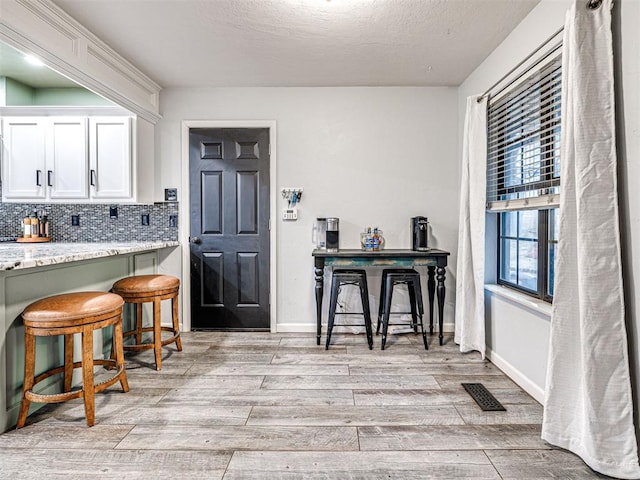 bar with a textured ceiling, visible vents, baseboards, decorative backsplash, and light wood finished floors