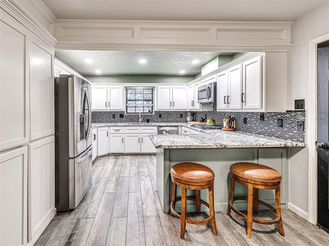 kitchen with stainless steel appliances, light wood-style flooring, decorative backsplash, white cabinetry, and a peninsula