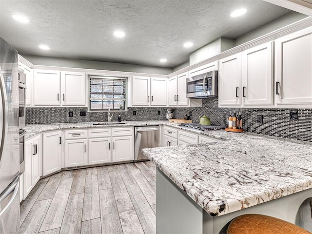 kitchen featuring a peninsula, appliances with stainless steel finishes, white cabinets, and a sink