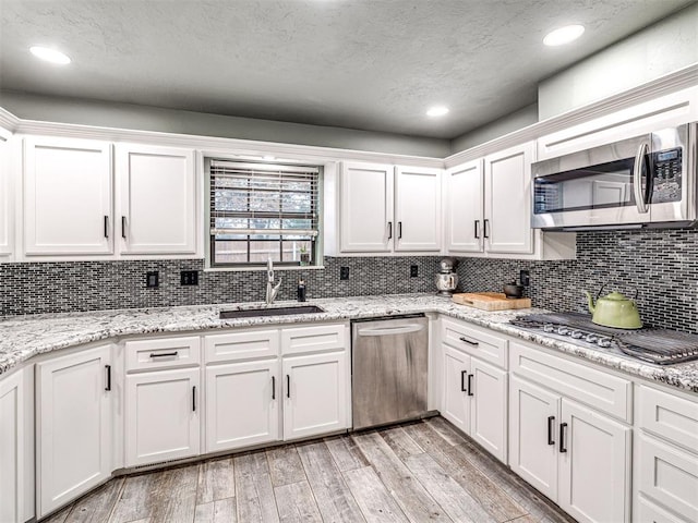 kitchen with light wood finished floors, stainless steel appliances, tasteful backsplash, white cabinetry, and a sink