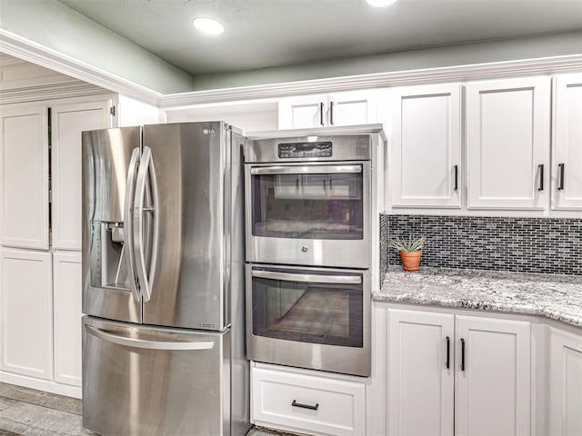 kitchen featuring wood finished floors, white cabinetry, appliances with stainless steel finishes, backsplash, and light stone countertops