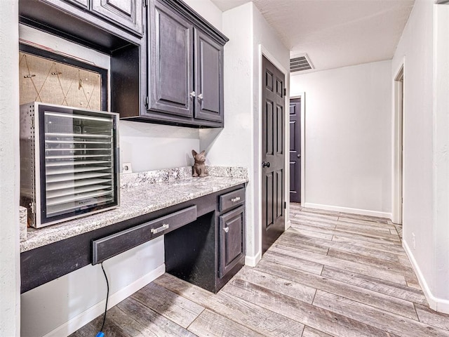 kitchen with built in desk, visible vents, light wood-style flooring, light stone countertops, and baseboards