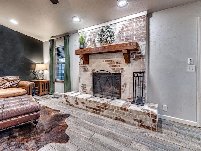 living area featuring a textured ceiling, a textured wall, a fireplace, wood finished floors, and baseboards