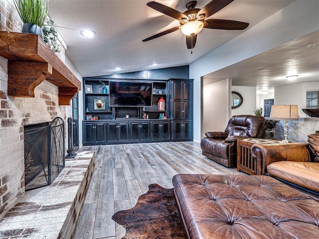 living area featuring a fireplace, light wood finished floors, lofted ceiling, ceiling fan, and a textured ceiling