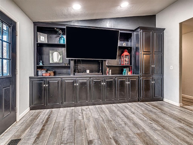 bar featuring light wood-style floors, baseboards, visible vents, and vaulted ceiling