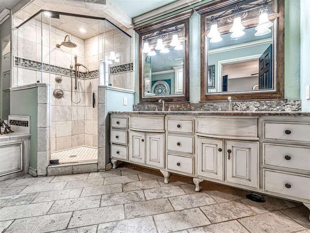 bathroom featuring a sink, double vanity, a shower stall, and stone tile floors