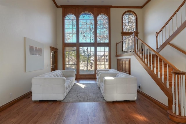 living room featuring wood finished floors, a towering ceiling, baseboards, stairs, and crown molding