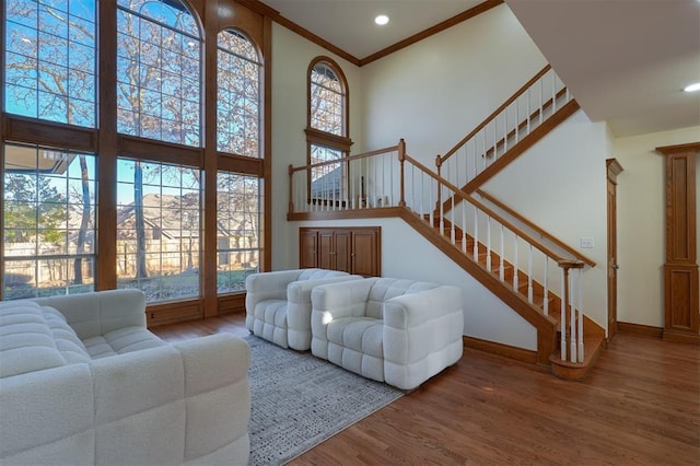 living area featuring wood finished floors, a towering ceiling, baseboards, stairs, and ornamental molding