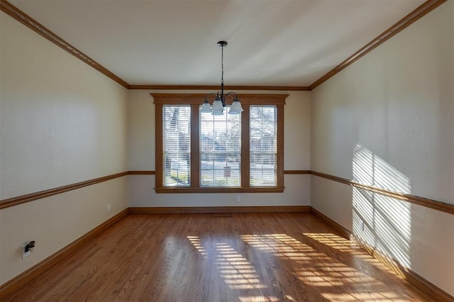 spare room with wood finished floors, crown molding, baseboards, and an inviting chandelier