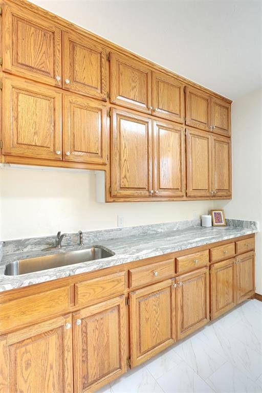 kitchen with marble finish floor, light countertops, a sink, and brown cabinetry