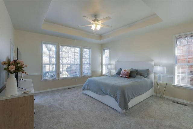 carpeted bedroom featuring a ceiling fan, visible vents, a tray ceiling, and baseboards