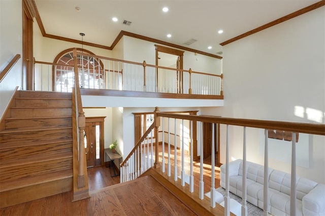 stairs featuring visible vents, crown molding, a high ceiling, and wood finished floors