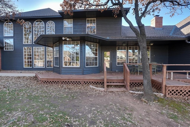 back of house with a chimney, a deck, and roof with shingles