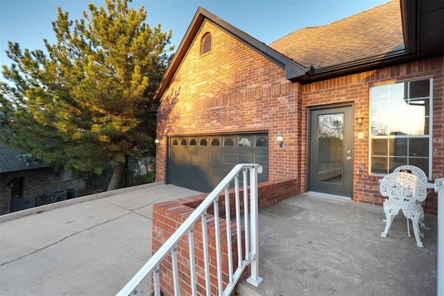 view of side of home with a shingled roof, brick siding, driveway, and an attached garage