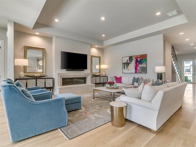 living room with visible vents, a tiled fireplace, wood finished floors, recessed lighting, and stairs