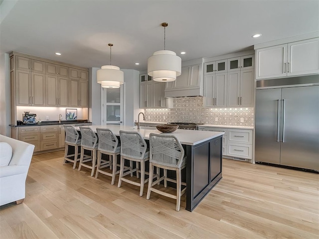 kitchen featuring tasteful backsplash, glass insert cabinets, premium range hood, stainless steel built in refrigerator, and light wood-type flooring