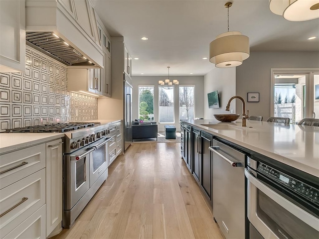 kitchen with a sink, custom range hood, high quality appliances, light wood-type flooring, and backsplash