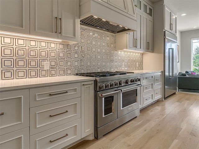 kitchen featuring decorative backsplash, high quality appliances, light countertops, and premium range hood