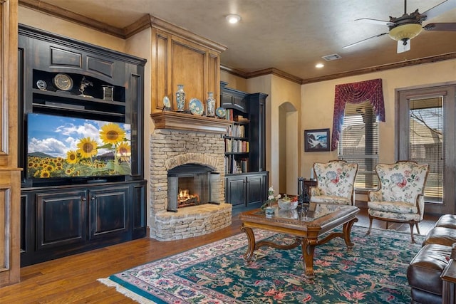 living area featuring arched walkways, crown molding, visible vents, wood finished floors, and a lit fireplace